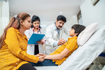 Indian doctor of pediatrician holding stethoscope checking heartbeat of sick boy kid at hospital wile her mother sitting by his side. health checkup, children medical insurance care.