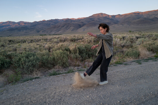 Bored hiker kicks up dust on side of gravel road in empty rural landscape