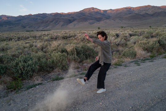Bored hiker kicks up dust on side of gravel road in empty rural landscape