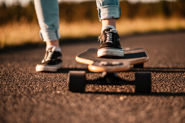 Woman rides at straight road on longboard at sunset time. Skater in casual wear training on board...