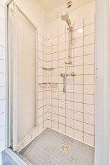 Shower faucets attached to tiled wall near glass partition and ornamental curtail in washroom at...