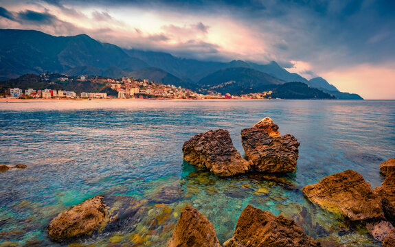 Big boulders on the Adriatic coast. Calm evening view of Potam Public beach. Illuminated cityscape of Himare town, Albania, Europe. Traveling concept background.
