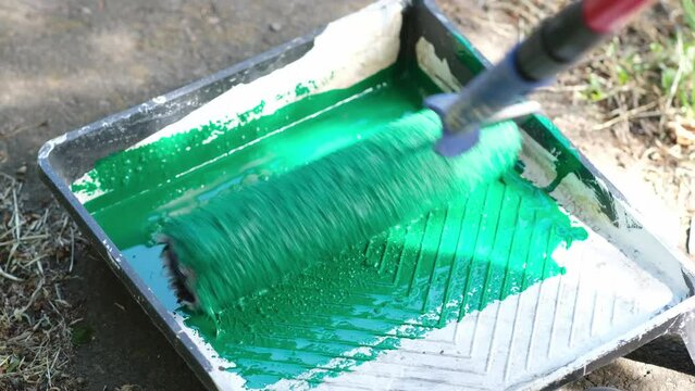 Dipping a roller into a plastic tray with green paint outdoors. House renovation, art wall painting. Tools for painting walls