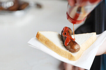 The humbe sausage sandwich or sausage in bread. Sang sanga. Traditional kids favorite at the bbq fundraiser with white bread and bright red tomato sauce or ketchup - obrazy, fototapety, plakaty