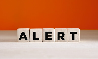 The word alert on wooden cubes on orange background with copy space.