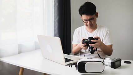 Content creator concept In virtual reality, an Asian man is looking down at a camera to edit on a laptop computer in his living room at home.