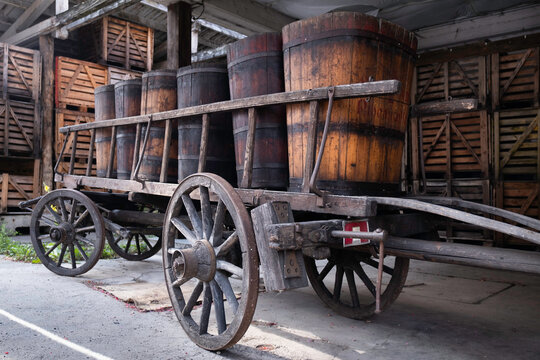 Old wooden wine barrels on a wooden cart in the french town of Ribeauvillé in Alsace. Crates in a barn in the background
