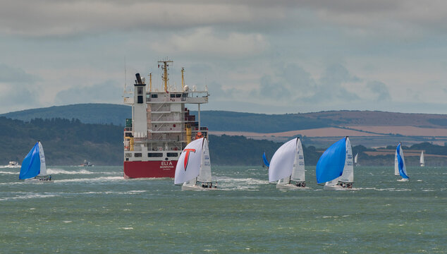 Solent, southern England, UK. 2022. Cowes week and racing yachts close to the container carrier ship Eli A on the Solent with a backdrop if the Isle of Wight coastline.