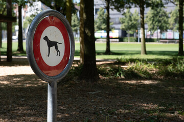 Sign 'Forbidden for dogs' in a park. The no-dog sign indicates that dogs are not allowed to stay in...