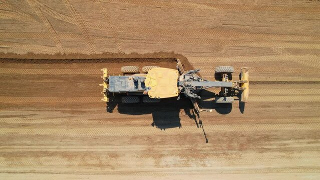 Road construction grader aerial view. The grader levels the sand for further road construction. Road construction works. Heavy machinery. Aerial footage.