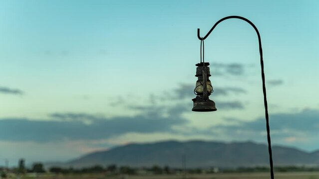 An antique lantern rusted and hanging on a hook with a blurred background of clouds at sunset - time lapse