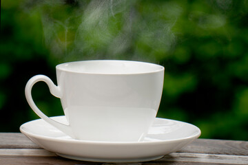 Hot Coffee Drink Concept, Hot ceramic white coffee cup with smoke on an old wooden table in a natural background.