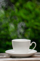 Hot Coffee Drink Concept, Hot ceramic white coffee cup with smoke on an old wooden table in a natural background.