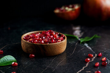 Pomegranate seeds in wood bowl with seeds on black marble table with pomegranate fruit on the background
