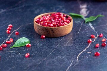 Pomegranate seeds in wood bowl with seeds on black marble table