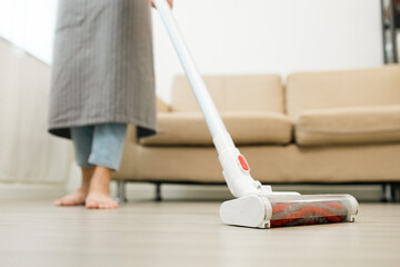Close up housewife using vacuum cleaner on the floor. Wearing an apron to clean the living room at...