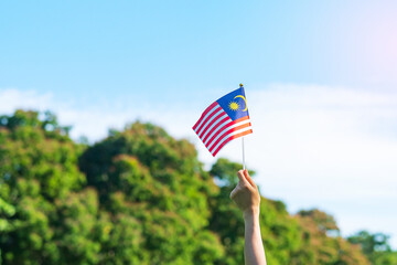 hand holding Malaysia flag on blue sky background. September Malaysia national day and August...