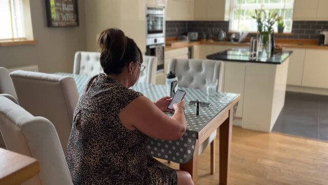 middle aged lady having a good time looking through her phone on social media in a large house in england