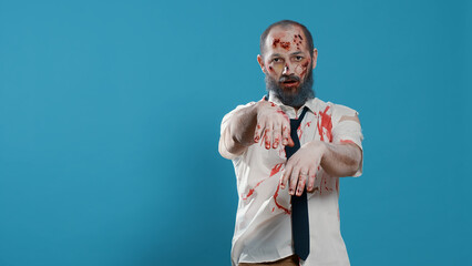Walking dead corpse with deep and bloody wounds standing on blue background. Horror looking...