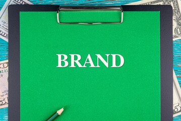 BRAND - word (text) and money bills, dollars on a green background notepad, pencil, wooden table. Business concept: buy, sell, commerce (copy space).