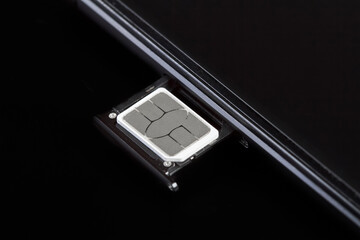 SIM card inserted into the sim card tray of a smartphone on dark background - obrazy, fototapety, plakaty