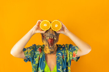 Unrecognizable woman in dinosaur mask holding as her eyes fresh orange slices. Surreal healthy food.