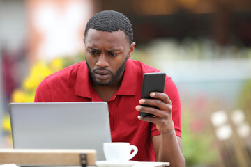 Worried black man using multiple devices in a bar