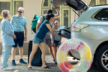 Big european family travelling on holiday trip, putting bags and trolley suitcase in automobile trunk before leaving on vacation. Child with parents and grandparents going on summer adventure. - obrazy, fototapety, plakaty