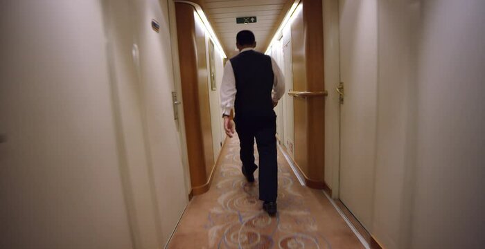 Wide Canted Following Shot Behind Male Cruise Ship Staff Walking In Hallway