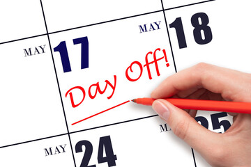 17th day of May. Hand writing text DAY OFF and drawing a line on calendar date 17 May. Vacation...