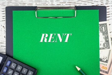 RENT - word (text) dollar bills on green background, pencil, calculator and wooden white table. Business concept: buying, selling, commerce (copy space).