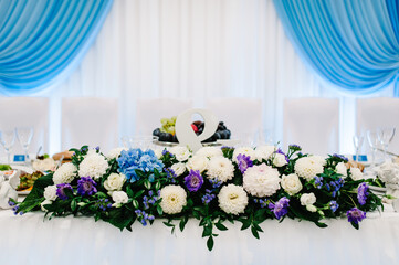 Festive table, arch, stands decorated with composition of flowers and greenery, candles in the banquet hall. Table newlyweds in the banquet area on wedding party. Stylish blue wedding.