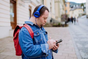 Happy young man with Down sydrome listening to music when walking in street.