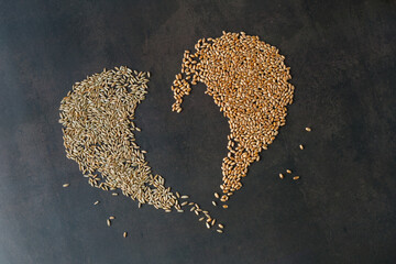 Natural dry rye and wheat  whole cereal grains in heart shape on dark grunge background.