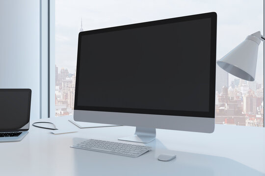 Close up of creative designer desktop with empty black mock up computer monitor laptop and supplies in modern office with window and panoramic city view. 3D Rendering.