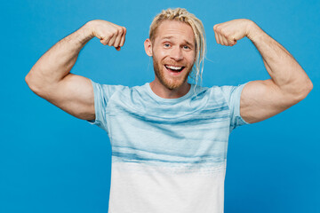 Young strong sporty fitness blond man with dreadlocks 20s he wear white t-shirt show biceps muscles on hand demonstrating strength power isolated on plain pastel light blue background studio portrait