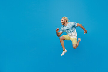Fototapeta na wymiar Full body side view sporty happy young blond man with dreadlocks 20s he wear white t-shirt jump high run fast isolated on plain pastel light blue background studio portrait. People lifestyle concept