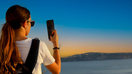 Back view of young tourist woman in  packpack using smartphone take picture at Sunset scene of...