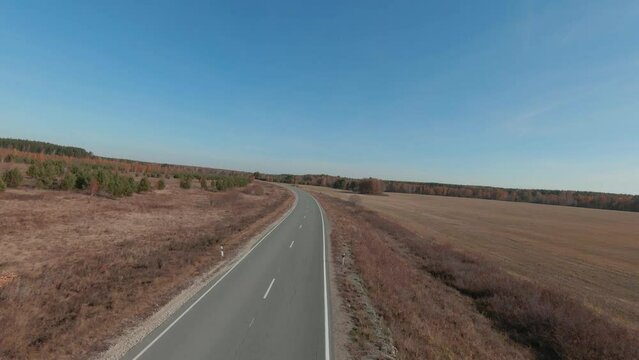 FPV drone high-speed flight along the road and fields in Ural, Russia. Beautiful autumn nature landscape at during daytime. Aerial view from a drone