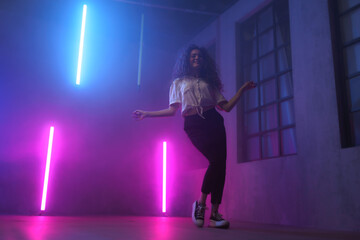 Portrait of a happy young woman dancing over neon light background at disco party