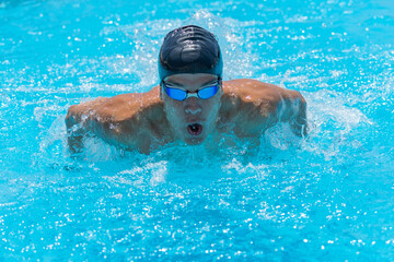 Close up action shot of athlete, young man, teenager swimming butterfly style. Sport, recreation concept. Selective focus.