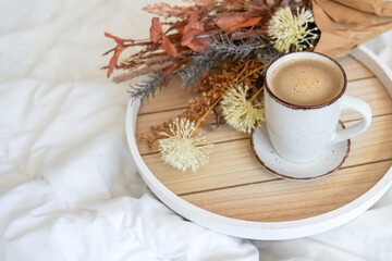 Cup of coffee cappuccino in bed on a white sheet of bedding linen with flowers. Cozy warm morning...