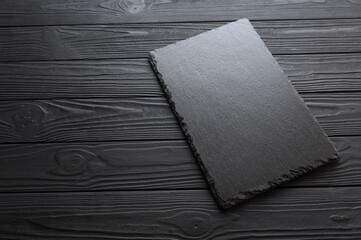 Black stone slate plate on a black stone background. Free copy space.