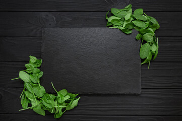 Kitchen table with stone cutting board, decorated with herbs. Presented on the black wooden background with center empty space. Table top view.