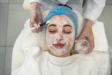 professional performs ultrasonic cleaning of the skin of the face with the help of a device.