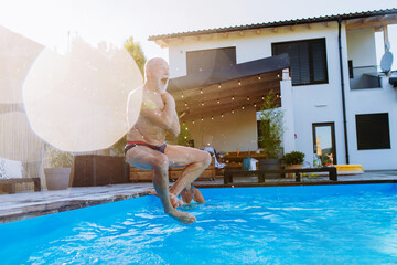 Happy senior man jumping into the swimming pool at backyard.