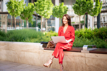 Full length of happy businesswoman using her laptop while sitting at the city park