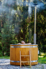 Young woman enjoying wooden bathtub with a fireplace to burn wood and heat water in backyard in...