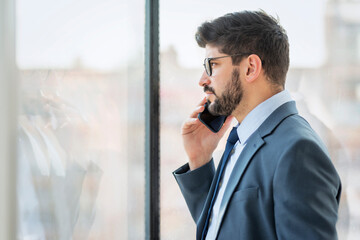 Executive businessman having a business call while standing by the window at a modern office