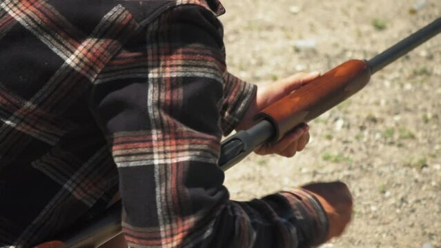 Man with checkered shirt loading pump action shotgun ammo from underneath